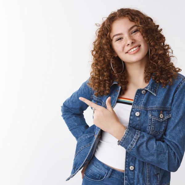 Charming joyful friendly ginger girl 20s freckles acne prone skin tilt head carefree inviting grab coffee together, pointing left smiling broadly introduce awesome copy space advertisement.